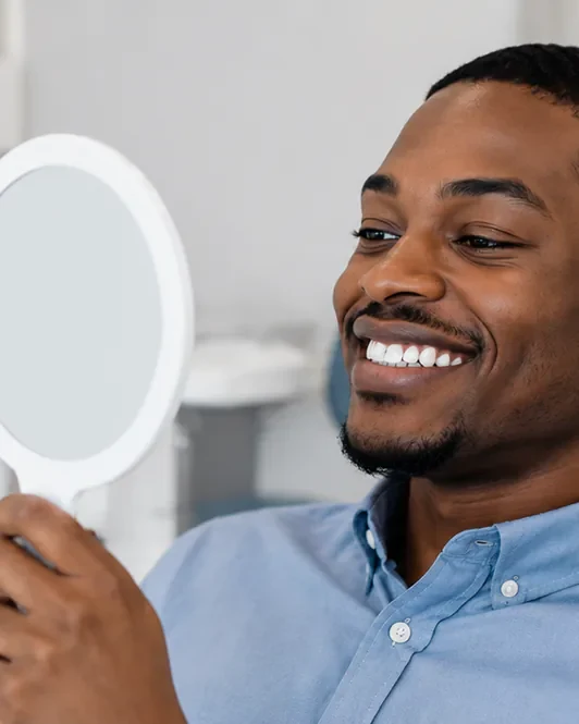 A man in the dental chair looking at his teeth in a hand mirror