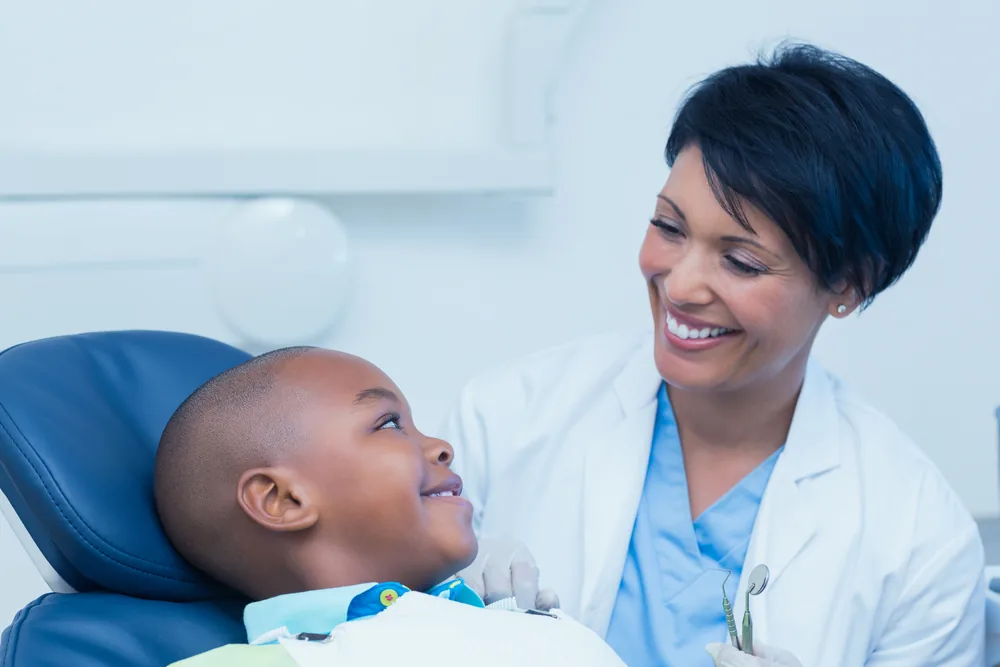 A smiling dentist talking with a young boy in the dental chair